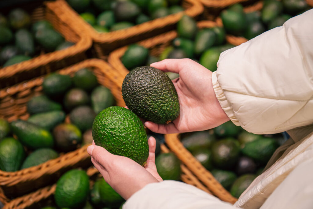 A woman chooses an avocado in a grocery store, close-up, buying organic food for cooking.
